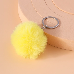 Detailed view of an 8cm lemon yellow faux fur pompom keychain on a geometric display