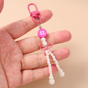 Porte-clés nœud rose avec perles et breloques boutons tenu sur un fond beige neutre