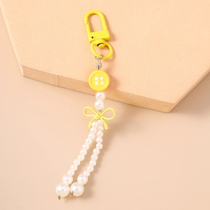 Détail du porte-clés à nœud jaune avec perles et breloque bouton sur support beige