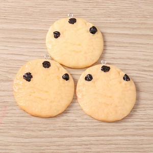 Detail of three resin chocolate chip cookie pendants with silver metal loops on wood