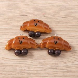 Macro view of three realistic croissant charms with cute faces and silver metal hooks