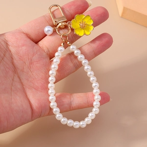 Detail of yellow flower keychain with white pearl loop strap and golden metal clasp
