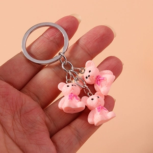 Trois adorables ours en résine rose sur un porte-clés en métal avec fond rose uni