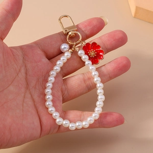 Detailed view of pearl keychain featuring a red enamel flower pendant and gold hardware