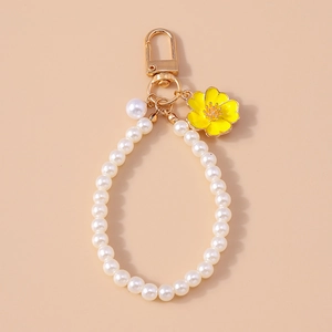 Detail of white pearl keychain with a yellow enamel flower pendant and golden lobster clasp