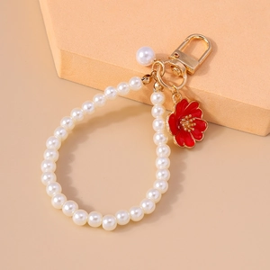 Close-up of pearl keychain with gold lobster clasp and red enamel flower charm