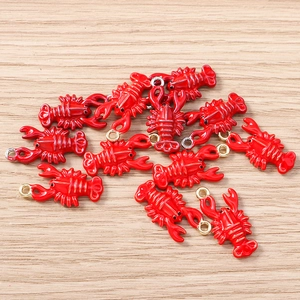 Macro detail of red enamel lobster charms with gold loops on a light wood surface
