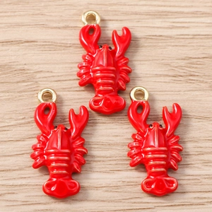 Macro view of three red lobster charms with gold loops on a light wood background