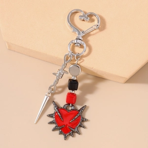 Gothic punk heart keychain with silver thorns and red heart pendant on beige background