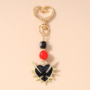 Gothic keychain detail with thorn heart pendant and red beads on beige background