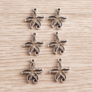Detailed macro view of six silver starfish pendants with dual hanging rings on wood