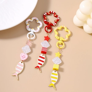 Three cute goldfish keychains with colorful heart beads and floral clasps on beige background