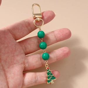 Detail showing hand holding Christmas tree keychain with green beads and gold ring