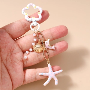 Détail du porte-clés marin avec dauphin rose, étoile de mer et perles à la main