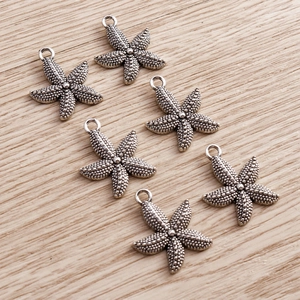 Detailed view of six vintage silver starfish pendants with textured finish on wood