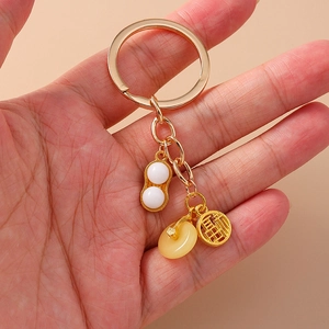 Porte-clés doré avec pendentif cacahuète et charme de caractère Fu tenu à la main