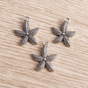 Macro view of vintage silver starfish charms with detailed dot texture and ring loops