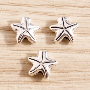 Three antique silver starfish charms for DIY jewelry making on light wood background