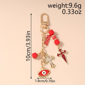 Detail of red Gothic cross sword and evil eye charms on a gold 2026 keychain