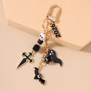 Detail of Halloween keychain with black bat charm, ghost pendant, and golden cross on a display