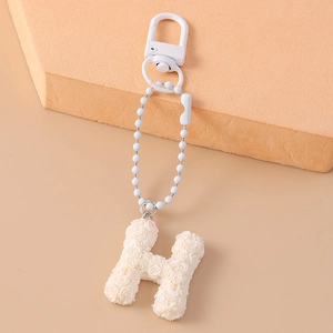 Close-up of white letter H keychain with embossed rose pattern and white metal chain