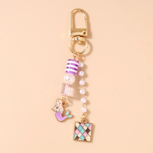 Détail du porte-clés sirène avec pompons dorés, perles et breloques violettes