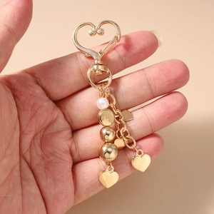 Détail d'un porte-clés en forme de cœur avec perles dorées et perle blanche à la main