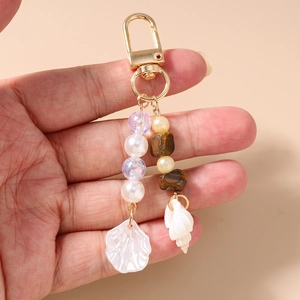 Detail of ocean-themed beaded keychain featuring white seashells and golden metal clasp