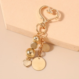Gros plan sur un porte-clés doré en forme de cœur avec perles et disques sur un socle beige
