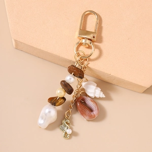 Detail of a gold marine-style keychain with starfish, pearls, and seashells on a beige stand