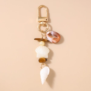 Detail of golden seashell keychain with natural cowrie shell and pearl bead