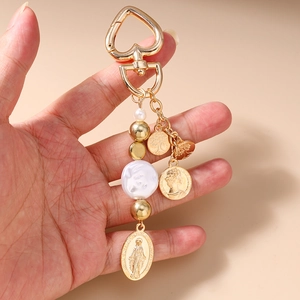 Golden keychain with heart clasp featuring religious pendants and pearls shown by hand