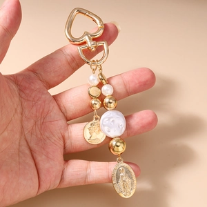 Detailed view of heart clasp, vintage coins and pearls on golden keychain accessory