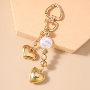 Détail d'un porte-clés cœur doré avec des perles sur un support géométrique beige