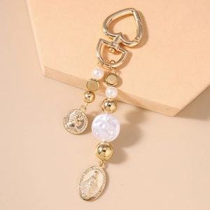 Close-up of golden heart clasp with faux pearl beads and embossed coin pendants on a keychain