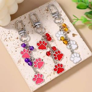 Pet paw print keychains with bells in pink, red, and white colors on a stone plate
