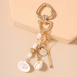 Detail of golden heart clasp keychain with pearls, sea shells and snake chain charm