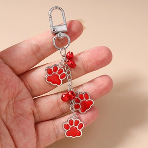Detail of hand holding silver keychain with three red paw charms and small bells