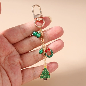 Détail d'un porte-clés de Noël avec cloche, arbre et couronne en alliage doré en main
