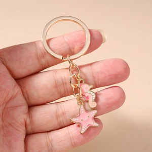 Close-up of golden keychain with pink enamel seahorse and starfish charms held in hand
