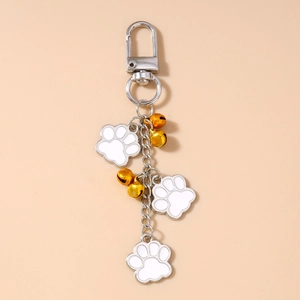 Detail showing white enamel cat paw charms and golden bells on a silver keychain
