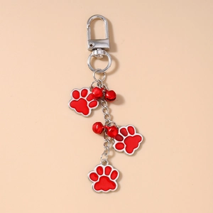 Detail of red enamel dog paw prints and metal bells on a silver keychain