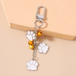 Detailed macro view of white enamel paw pendants and gold bells on a silver keychain