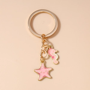 Detailed close-up of seahorse and starfish charms on a gold keychain with pink enamel