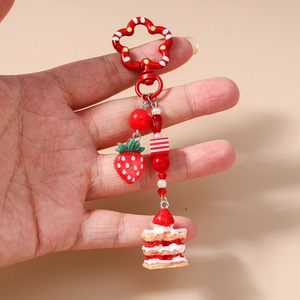 Detail of a strawberry cake keychain featuring red bead charms and resin pendants