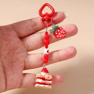 Macro detail of red beaded keychain with strawberry cake pendant and heart metal hook