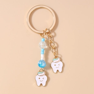 Close-up of golden alloy keychain featuring cute tooth charms with pink and mint green beads
