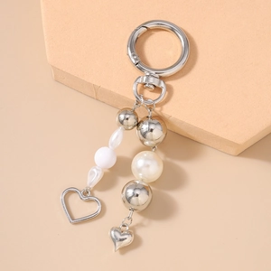 Close-up of pearl bead keychain with silver heart pendants and metal clasp on beige background