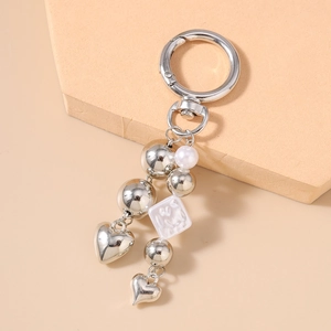 Detail of silver heart keychain with white pearls and metal beads on neutral background