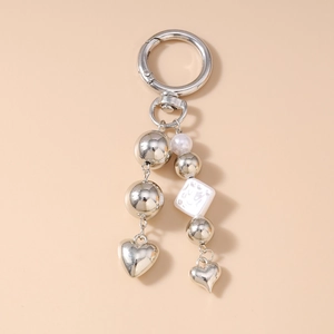 Detail of silver heart keychain with pearl beads and dual tassels on a soft beige background